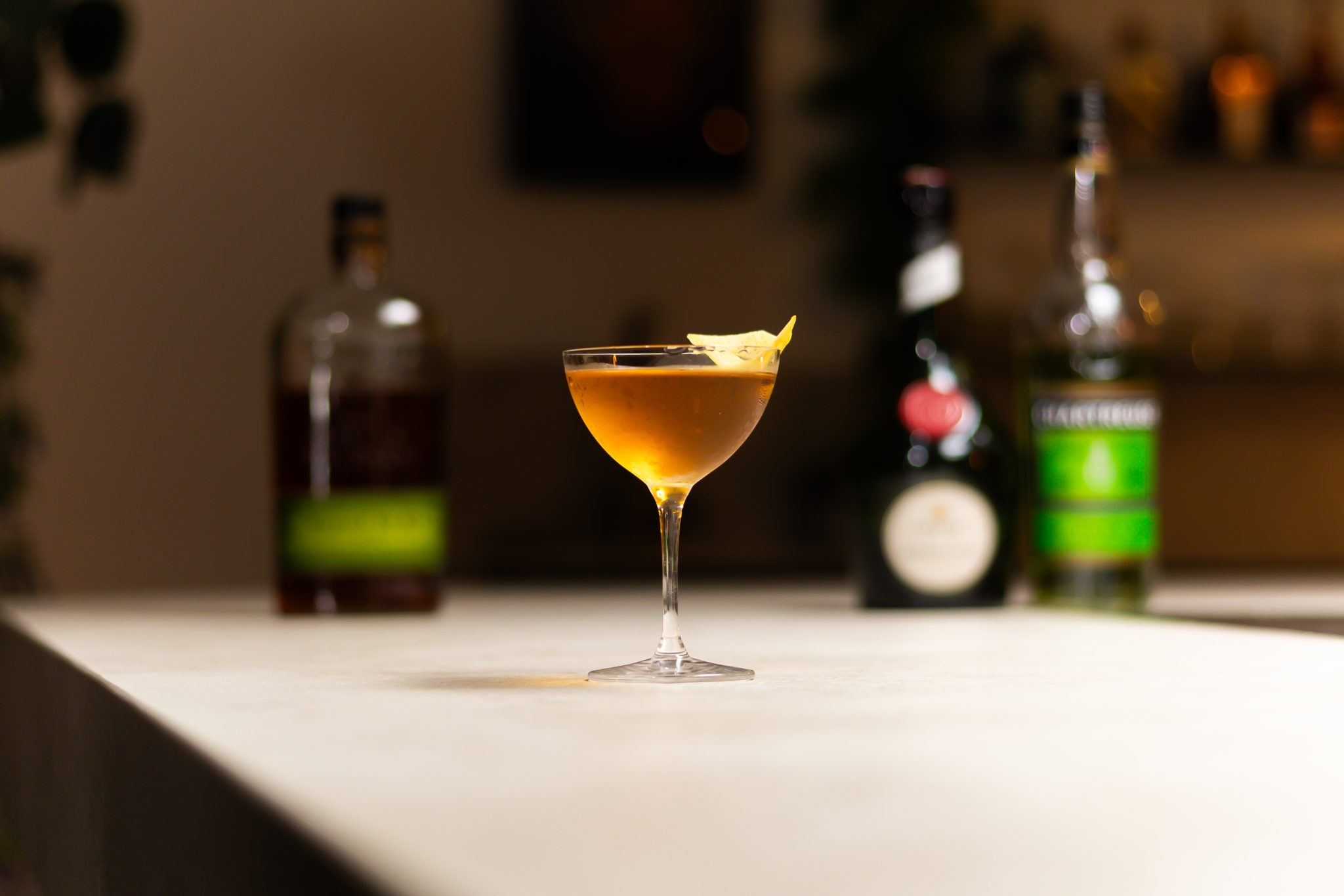 Rye whiskey, Bénédictine, and green Chartreuse laid out on a white bar table