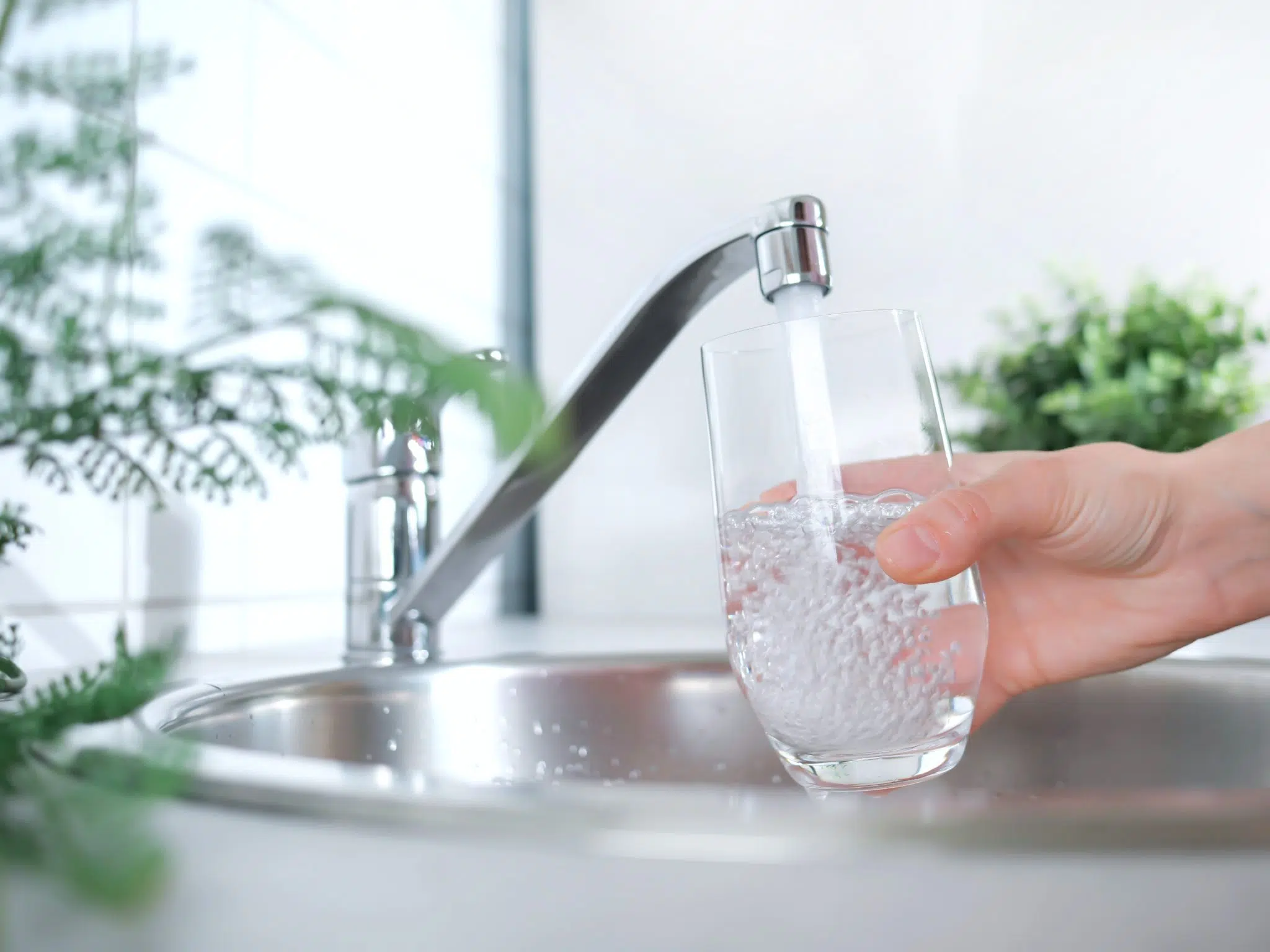 A shot of a highball glass holded under the water tap and filling it with cold water