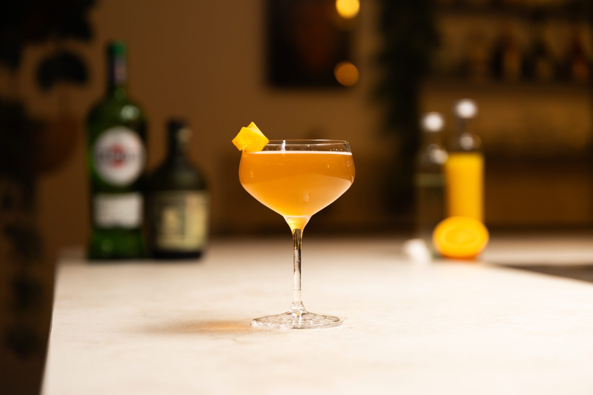 Dry vermouth, dark rum, orange juice, orange, rich sugar syrup and sugar cubes laid out on a white bar table