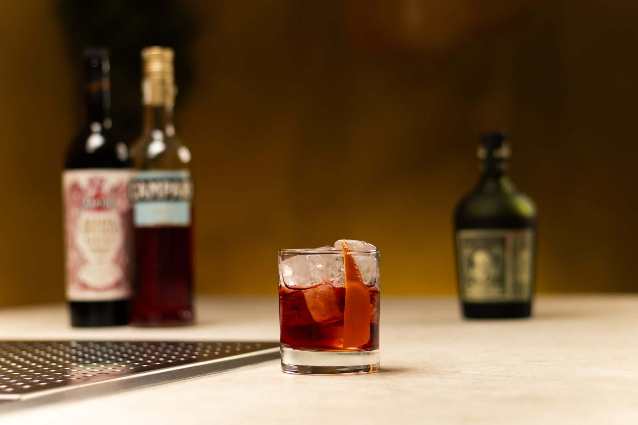 Dark Rum, Campari, and sweet Vermouth laid out on a white bar table