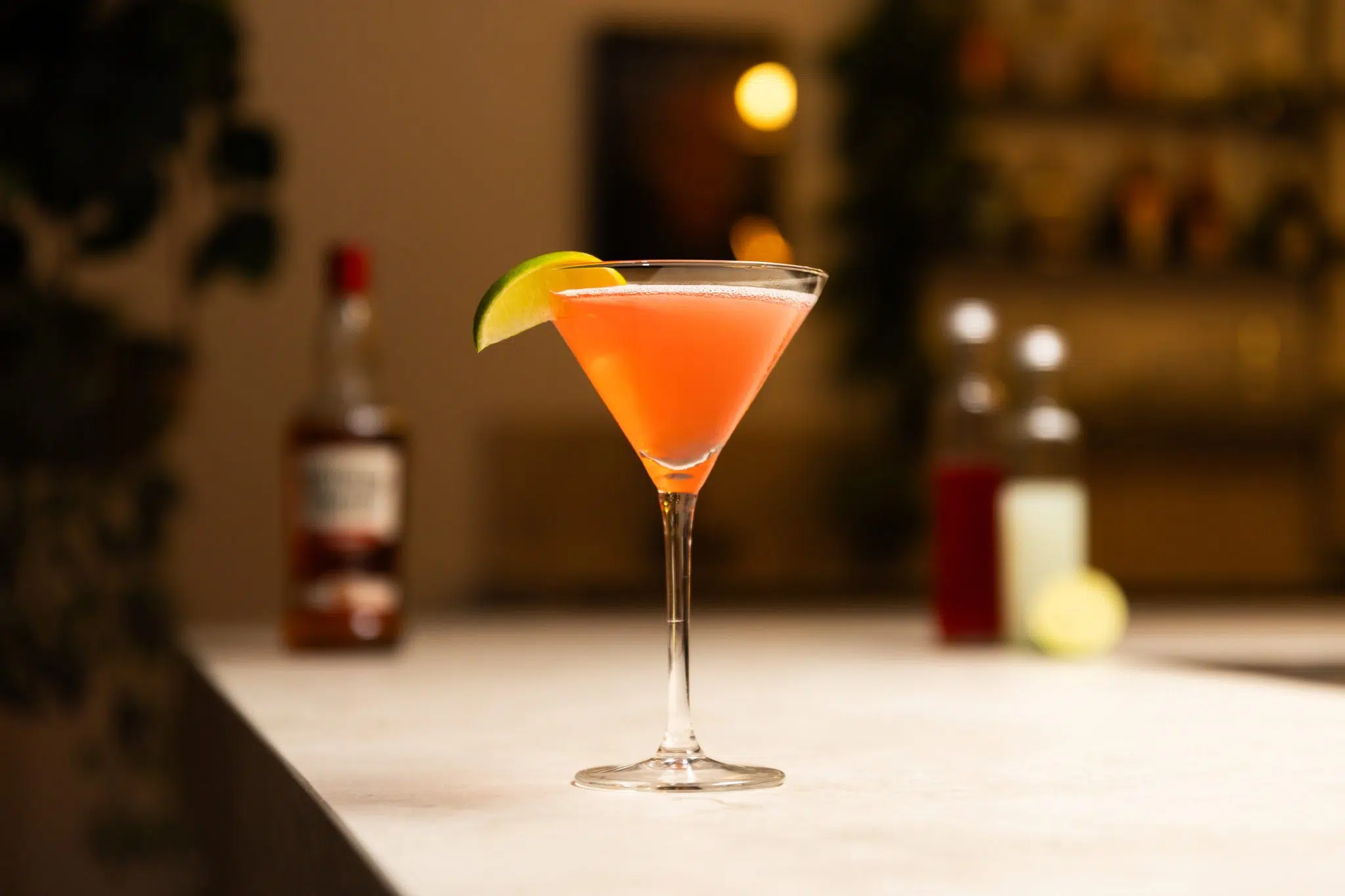 Southern Comfort, cranberry juice, lime juice, and lime laid out on a white bar table