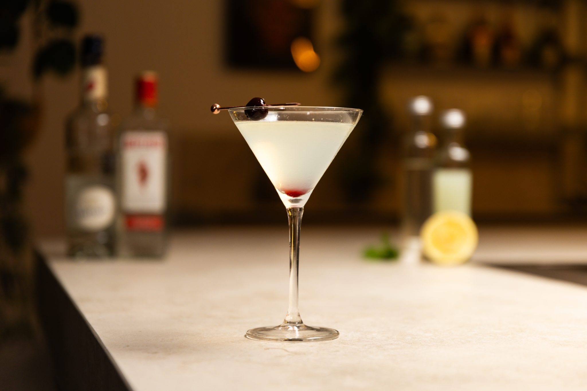 Gin, lemon juice, lemon, maraschino liqueur, mint, sugar cubes and simple syrup laid out on a white bar table