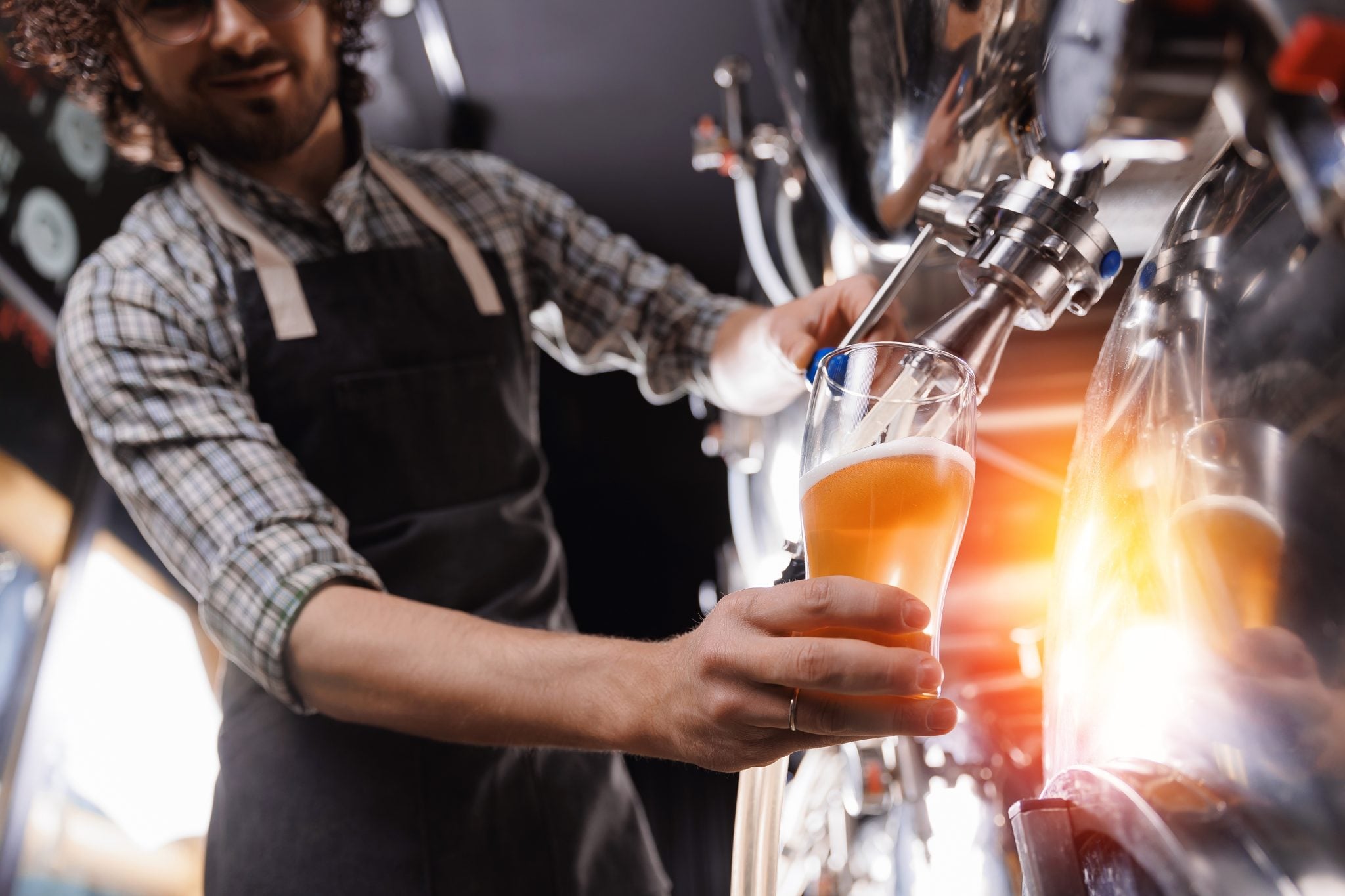A shot of a Cicerone pouring beer in a pint glass in a brewery