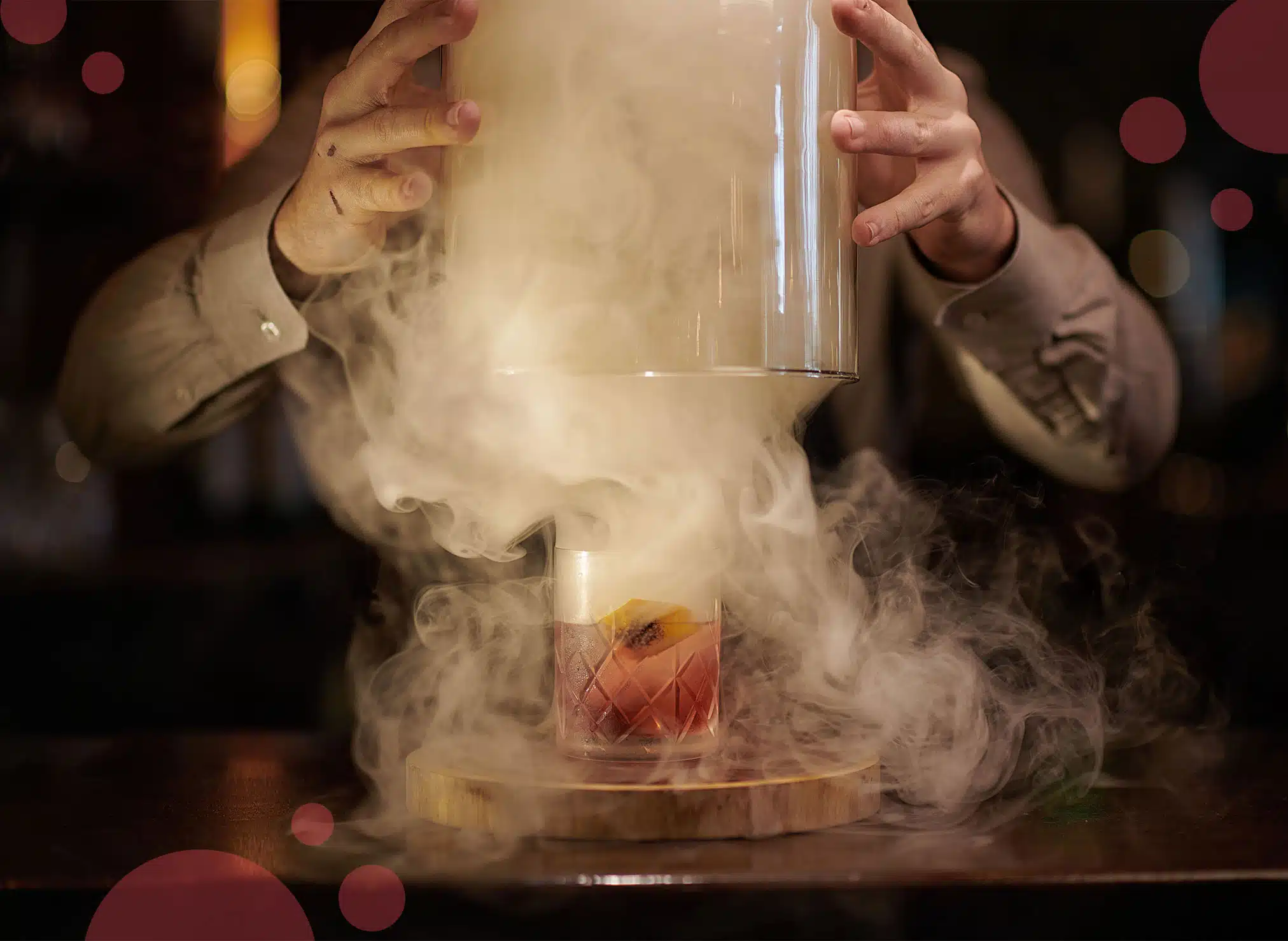 Crystal lid on a wooden tray being lifted releasing a lot of smoke and showing an old-fashioned glass with spirit in it.