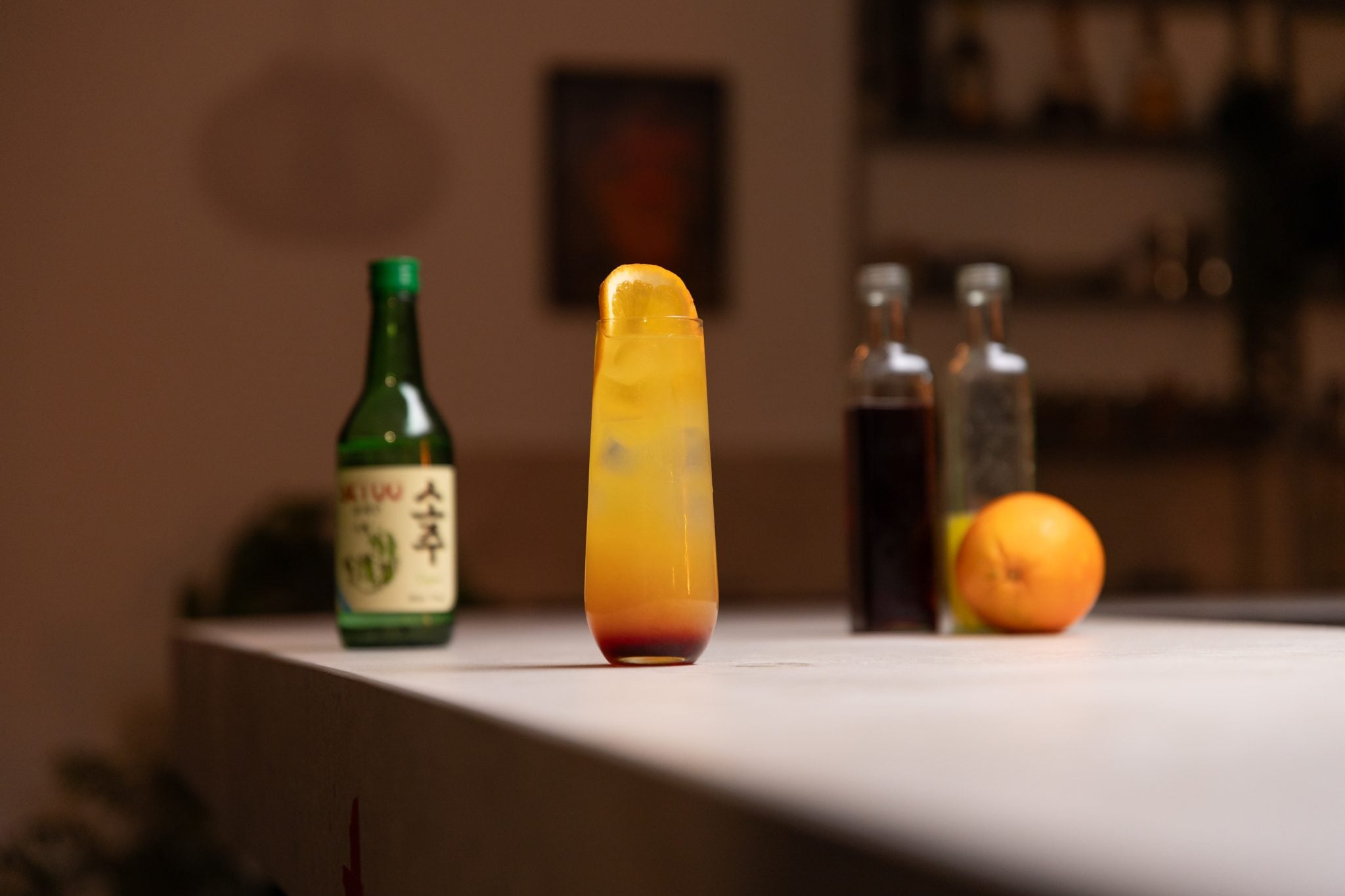Soju, grenadine, orange juice and orange laid out on a white bar table