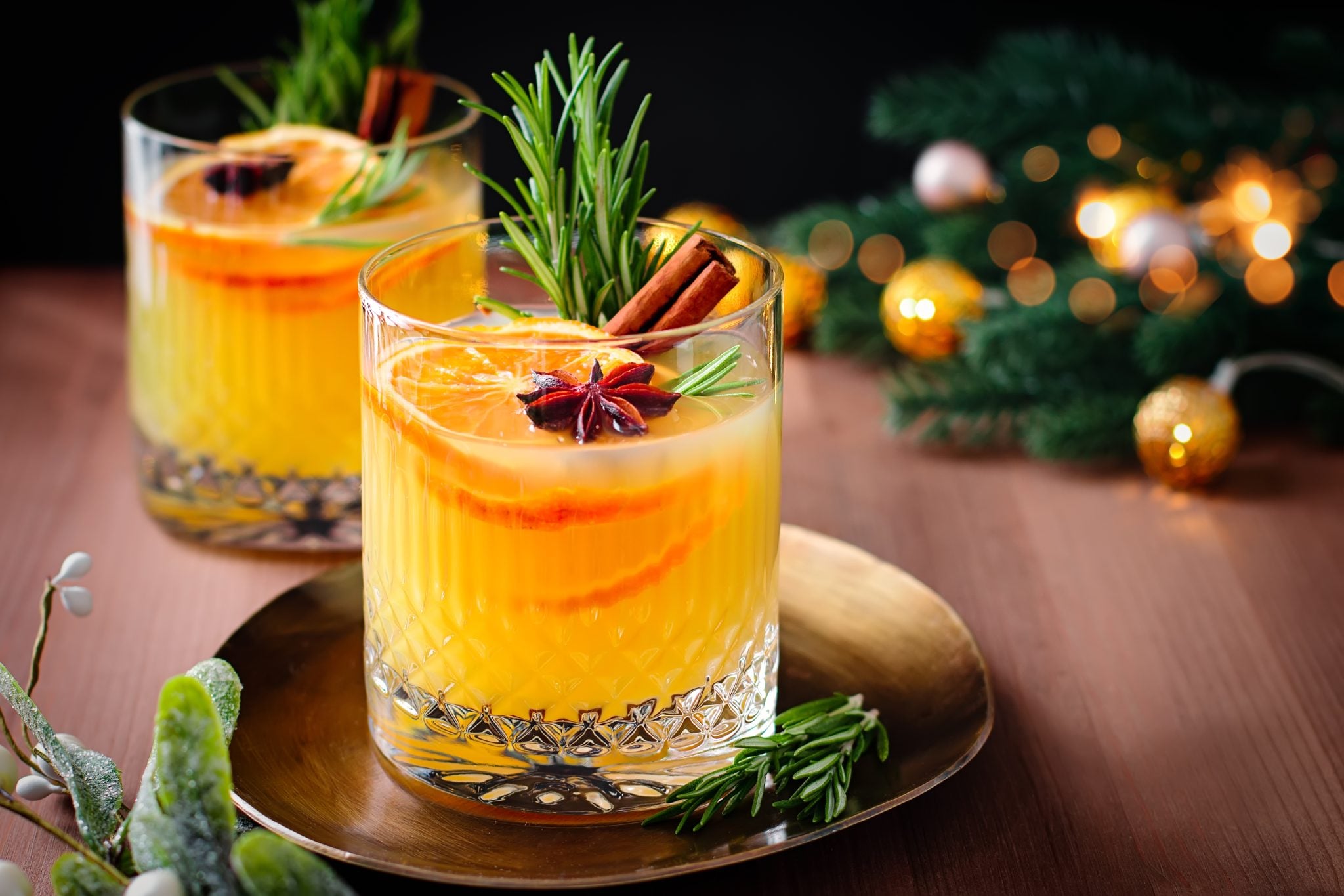 A shot of two Spiced Old Fashioned cocktails in Old Fashioned glasses surrounded by christmass decoration