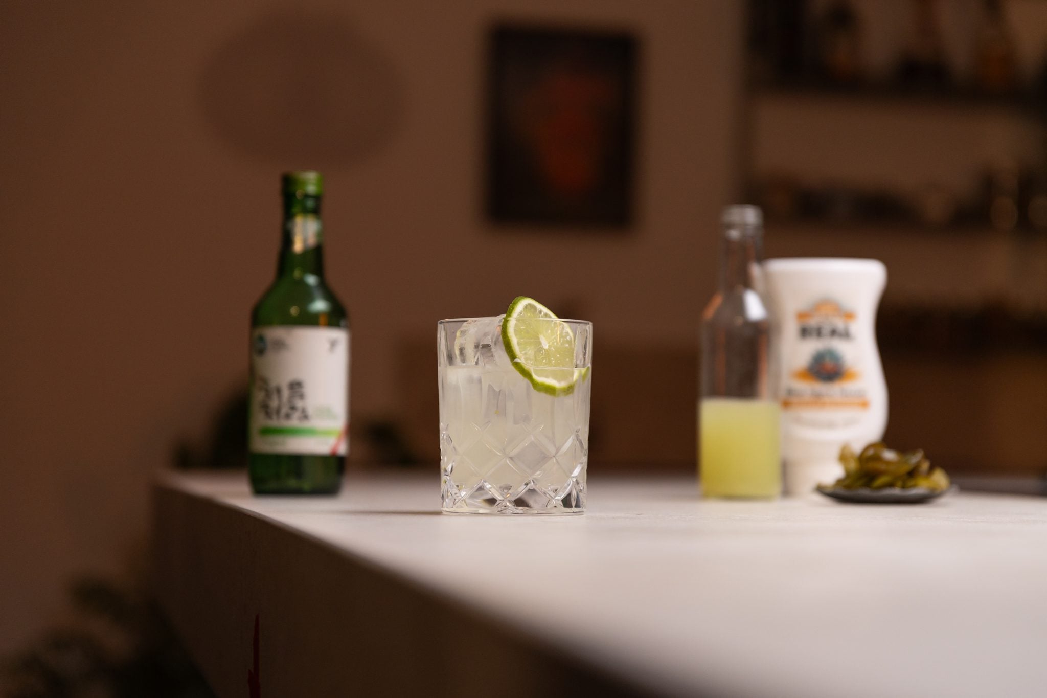 Soju, lime juice, agave syrup, and jalapeños slices laid out on a white bar table