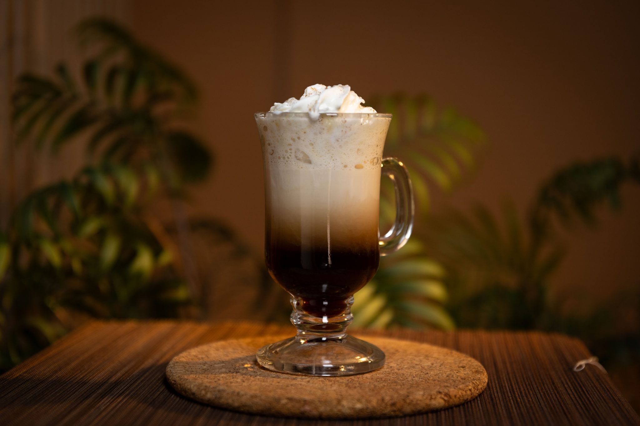 A side shot of a Spiked Pumpkin Spice Latte cocktail in a mug on a cork coaster placed on a brown placemat