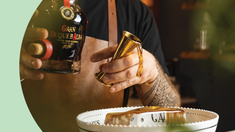 A shot of a bartender pouring a liquor with a jigger into a punch bowl on a huge ice cube