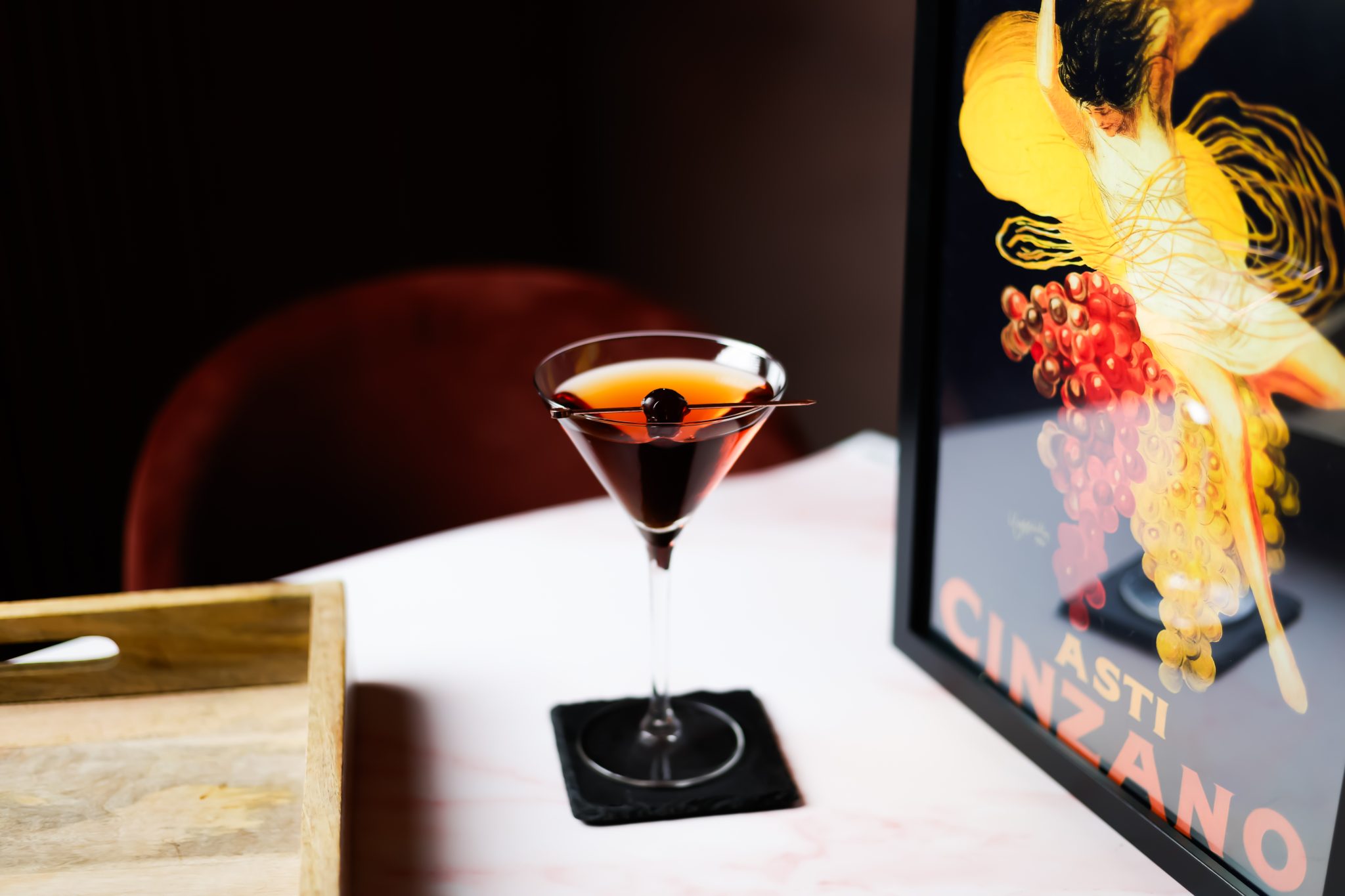 A side shot of a Star cocktailin a martini glass on a black stone coaster placed on a white surface with a wooden tray and a frame on the sides