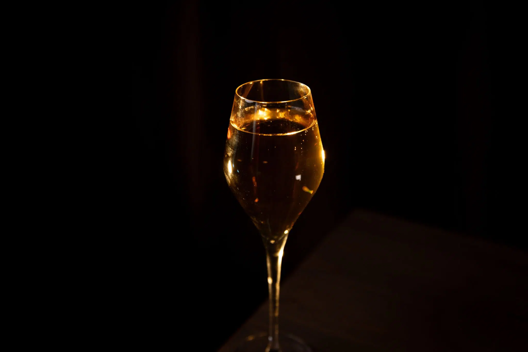 A side shot of a Sticky Toffee Fizz cocktail in a flute glass on a black background