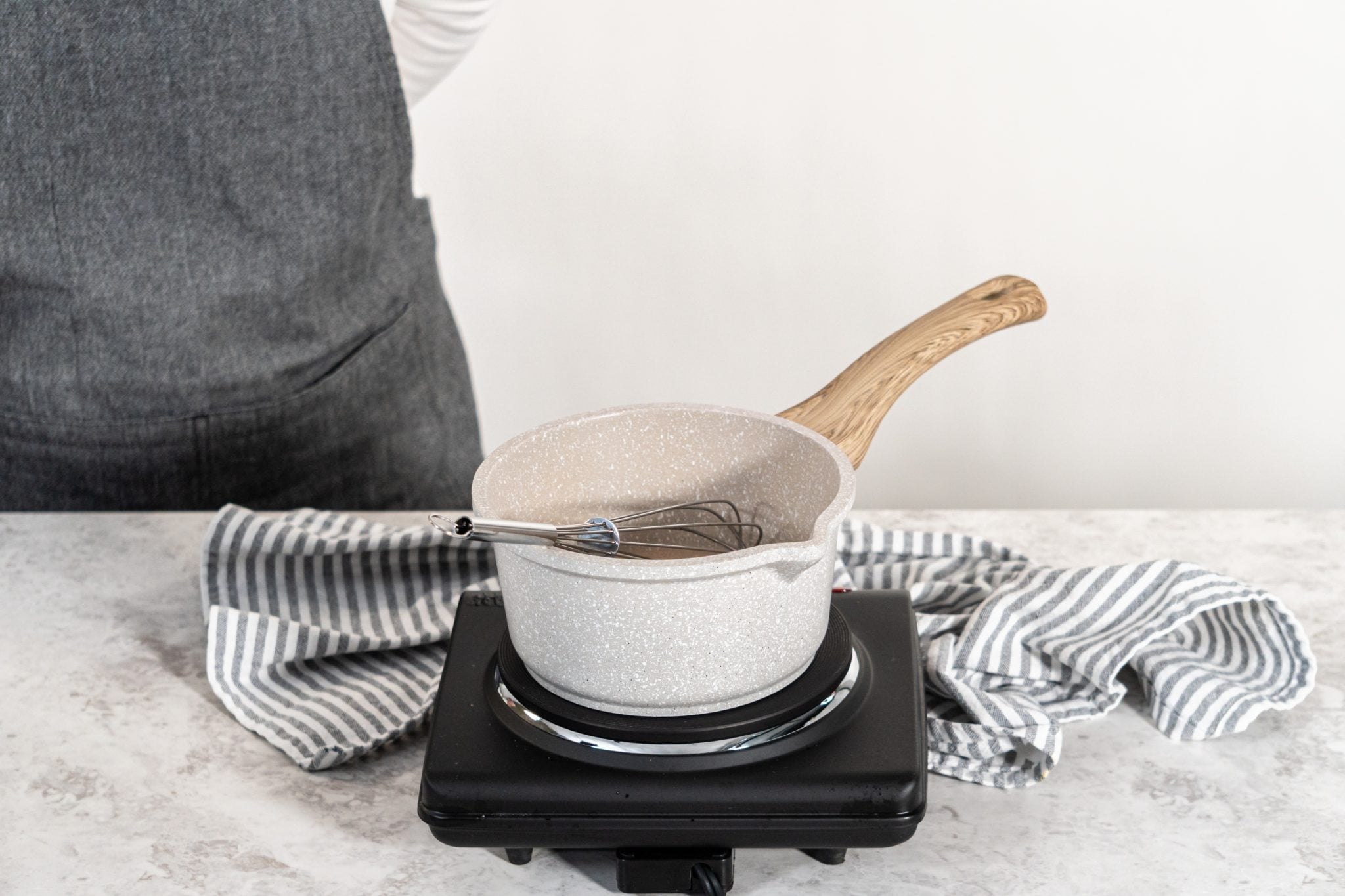 A shot of a white top on a stove with simple syrup inside placed on a white surface