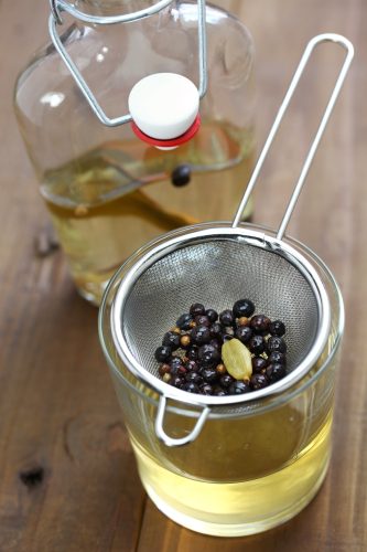 A shot of the straining process of an infused gin using a fine strainer and a glass