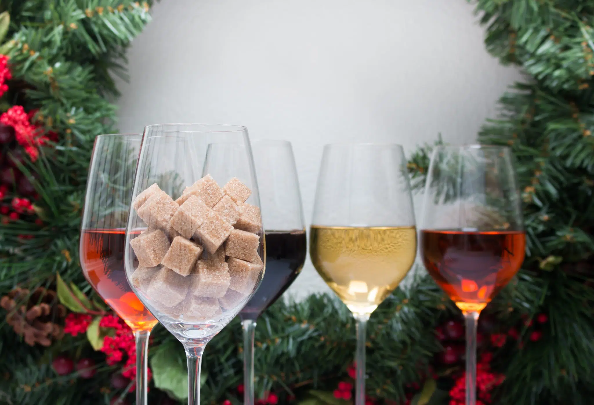 A shot of five wine glass filled with brown sugar cubes, and four different dessert wine types