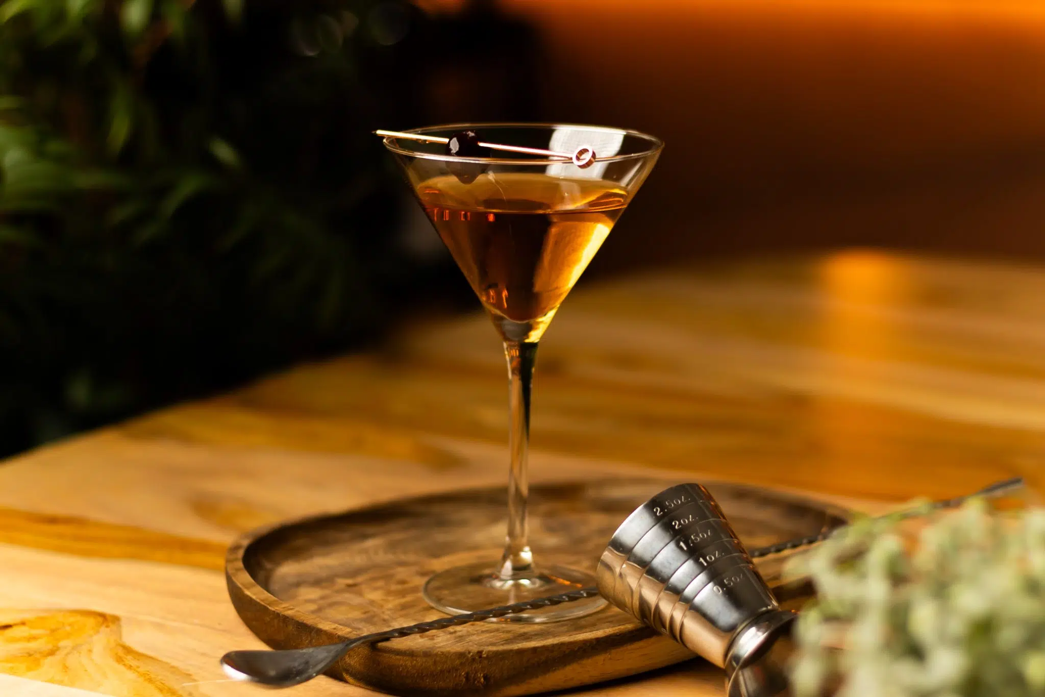 A side shot of a Sweet Martini cocktail in a martini glass on a wooden board placed on a wooden table with a bar spoon and a jigger around