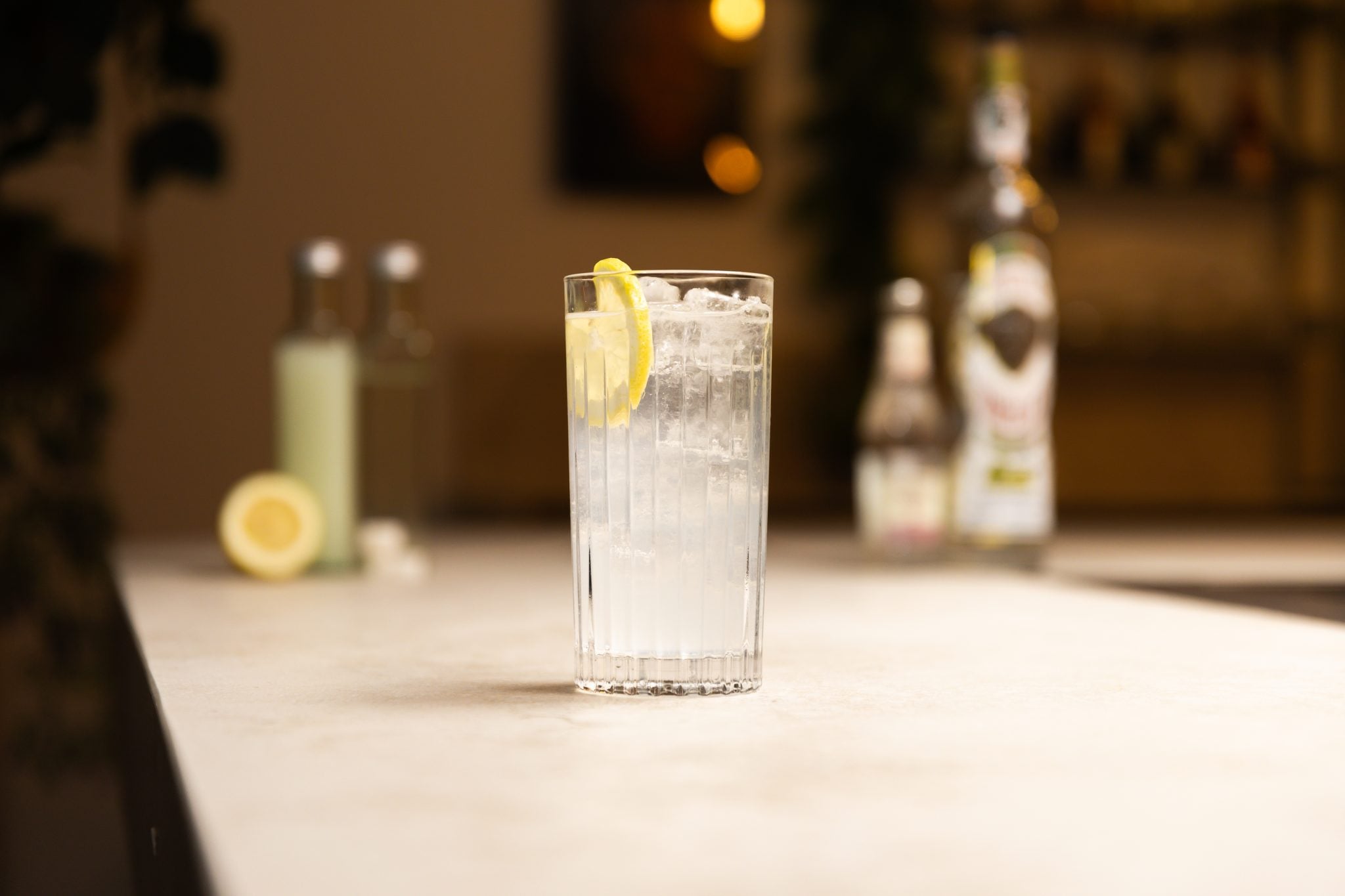 Tequila, soda, lemon juice, simple syrup, lemon and sugar cubes laid out on a white bar table