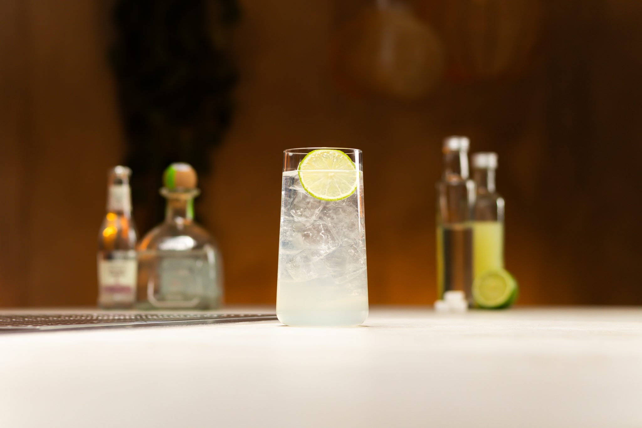 Silver Tequila, lime juice, simple syrup, soda, sugar cubes and lime laid out on a white bar table