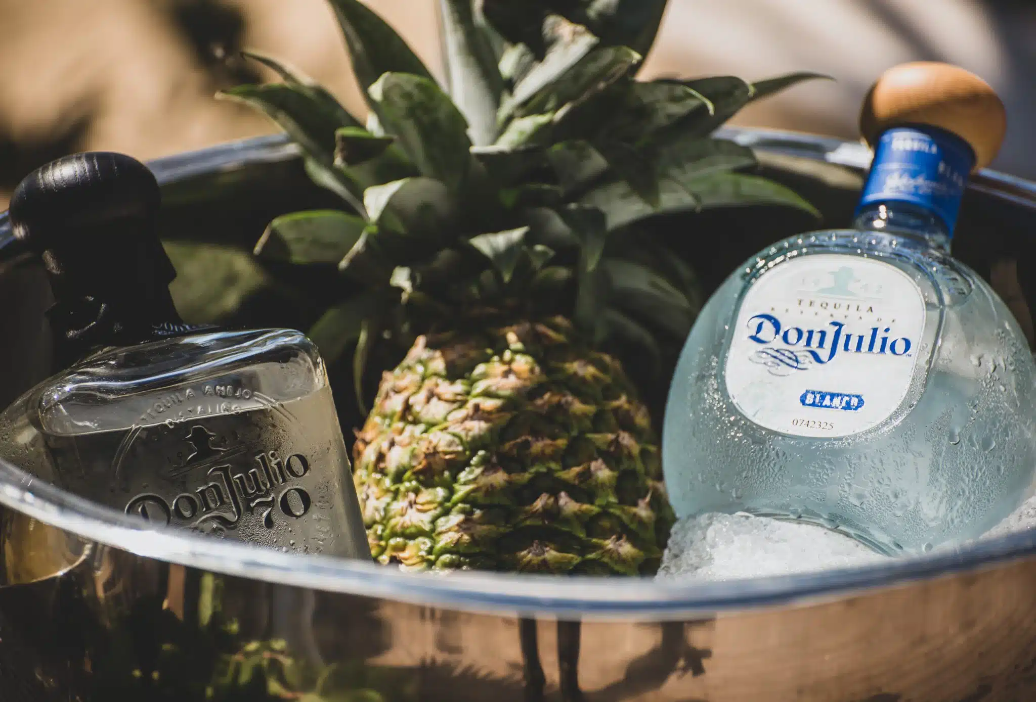 Two bottles of Don Julio tequila in an ice bucket with a pineapple.