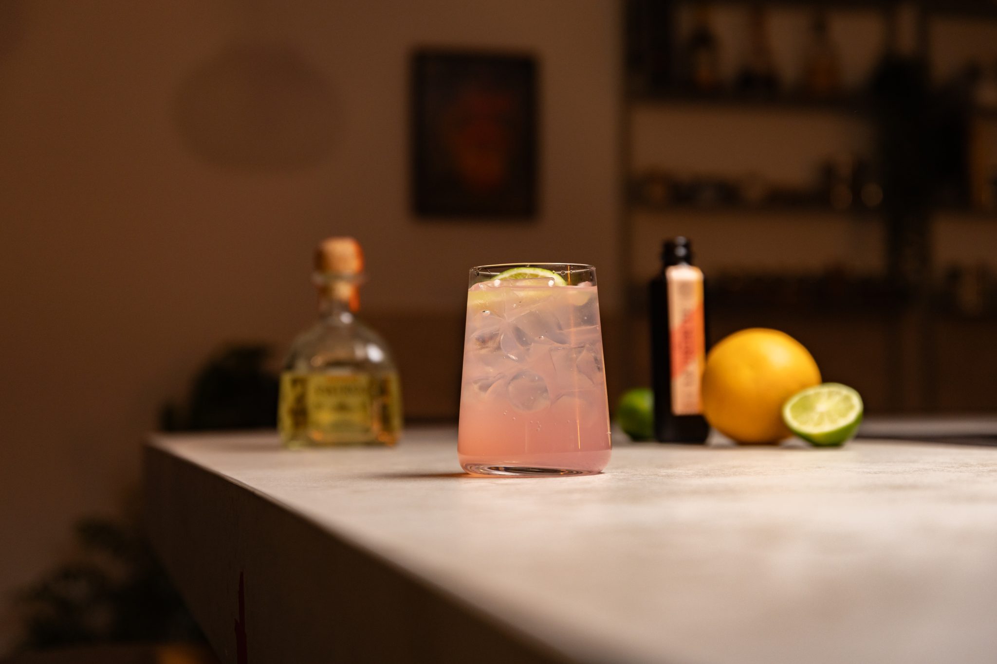 Tequila, grapefruit soda, lime and orange laid out on a white bar table