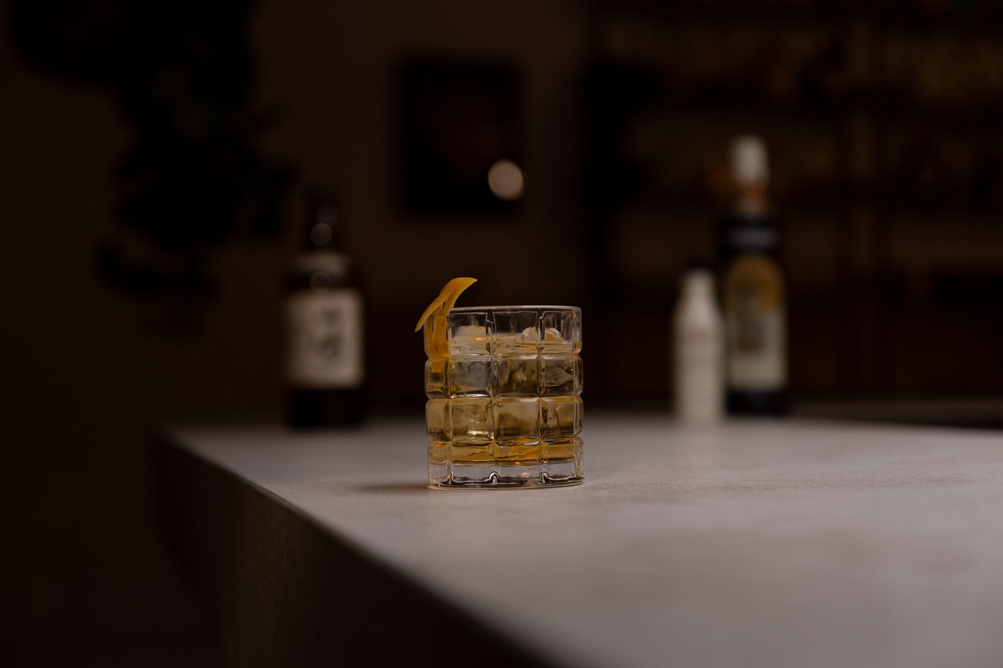 Japanese whisky, smoky syrup, and cacao bitters laid out on a white bar table