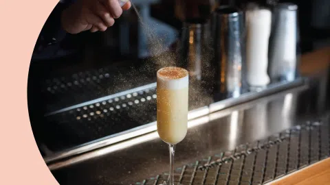 A shot of a bartender dusting a cocktail on a bar table