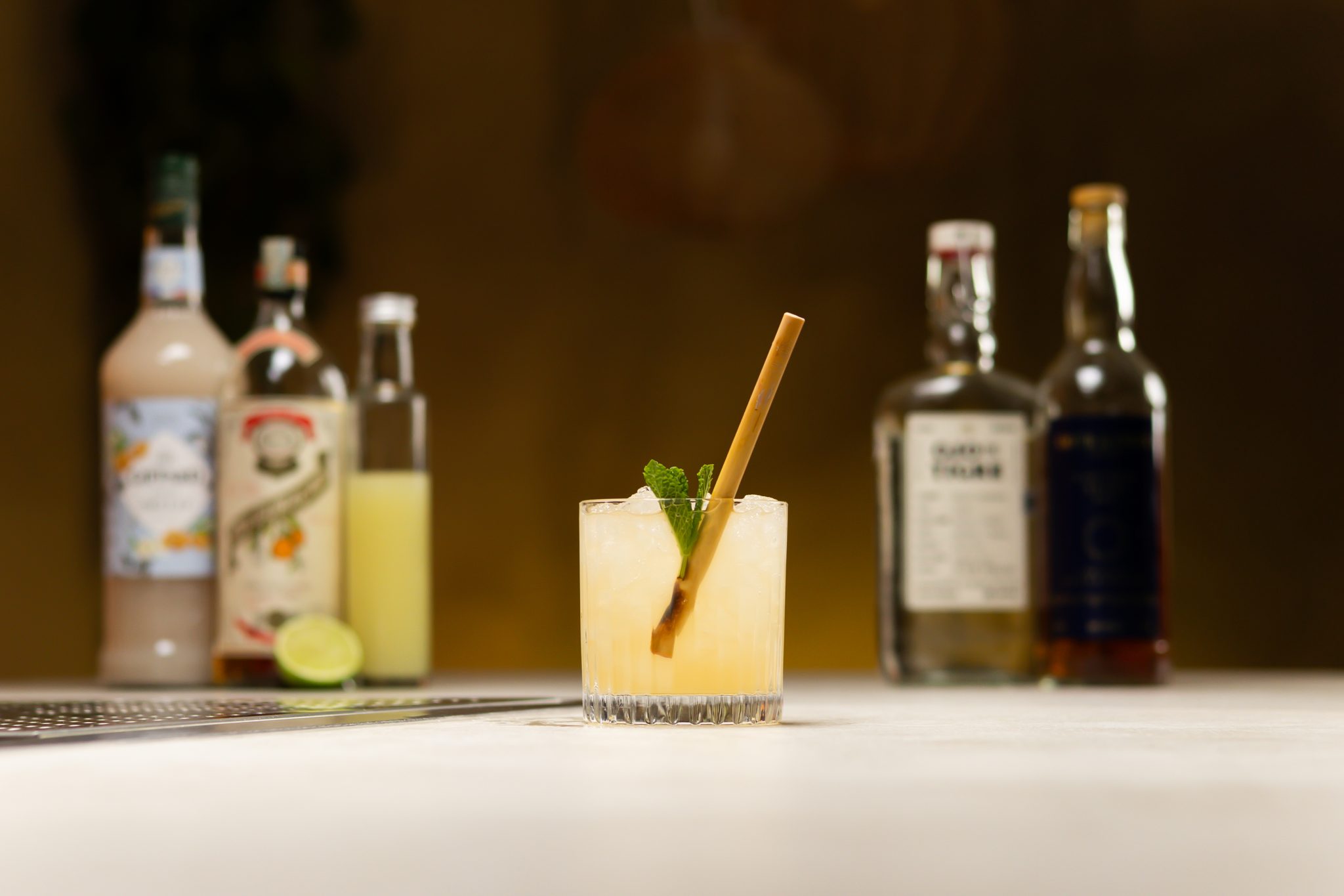 Mezcal, Jamaican Rum, orgeat syrup, lime juice, and orange curacao laid out on a white bar table