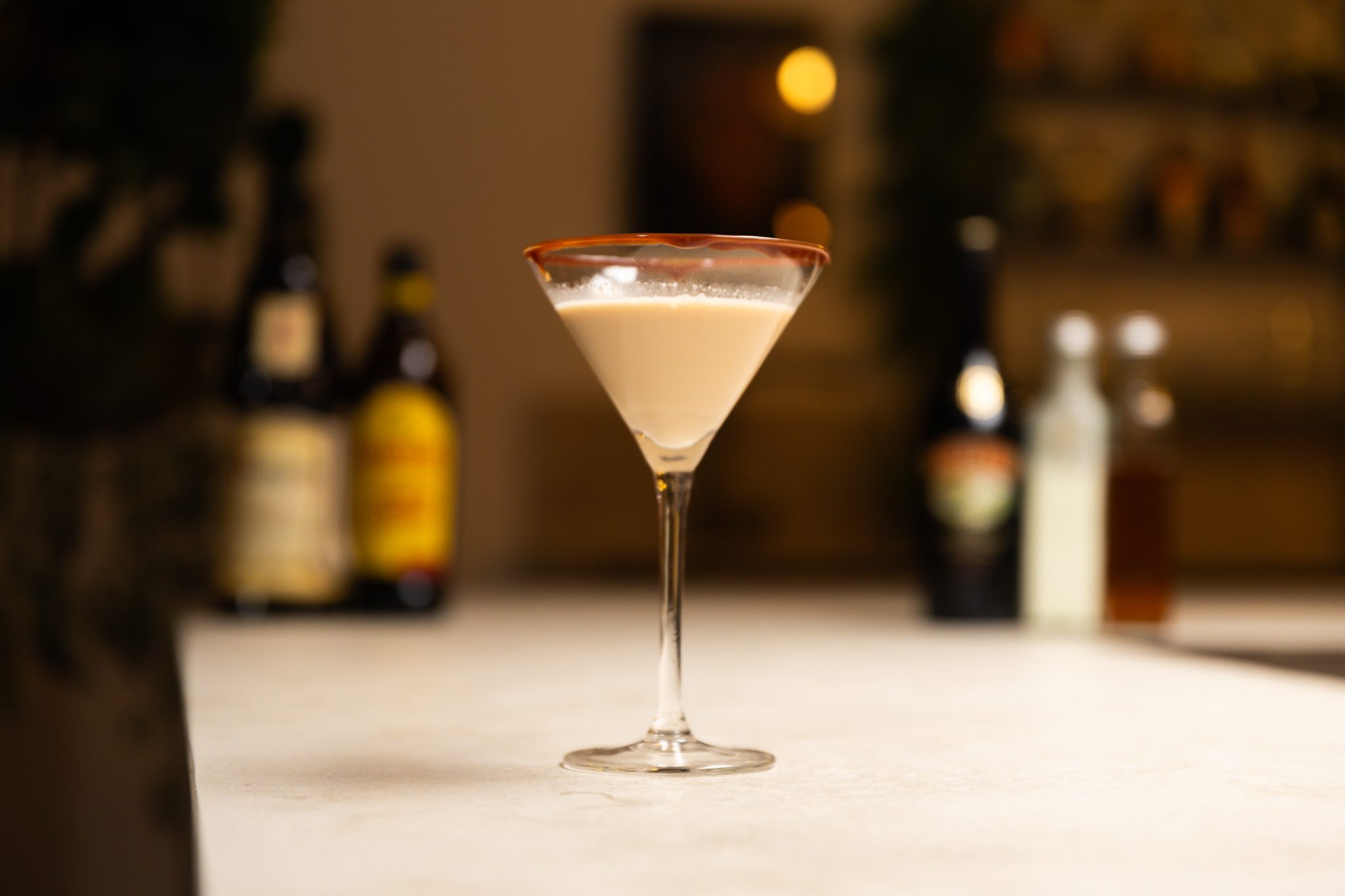 Baileys Irish Cream, Kahlua, Frangelico, honey syrup, heavy cream, and Toblerone laid out on a white bar table