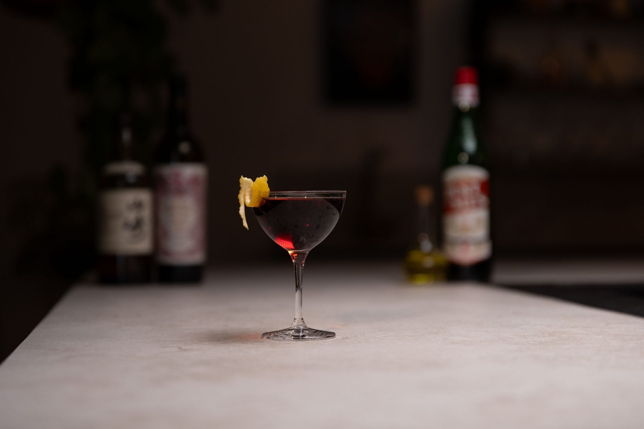 Single Malt Japanese Whisky, sweet vermouth, vermouth amaro, and Strega liqueur laid out on a white bar table