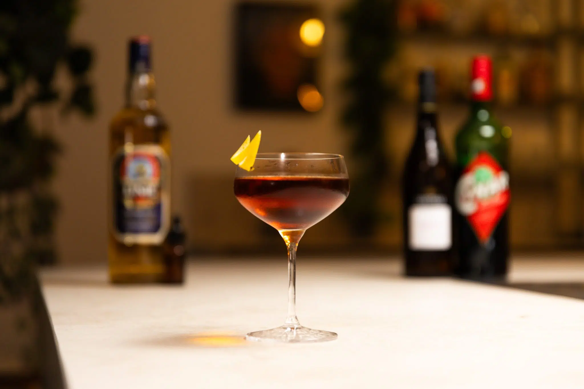 Peach bitters, Cynar, Manzanilla Sherry, and aquavit laid out on a white bar table