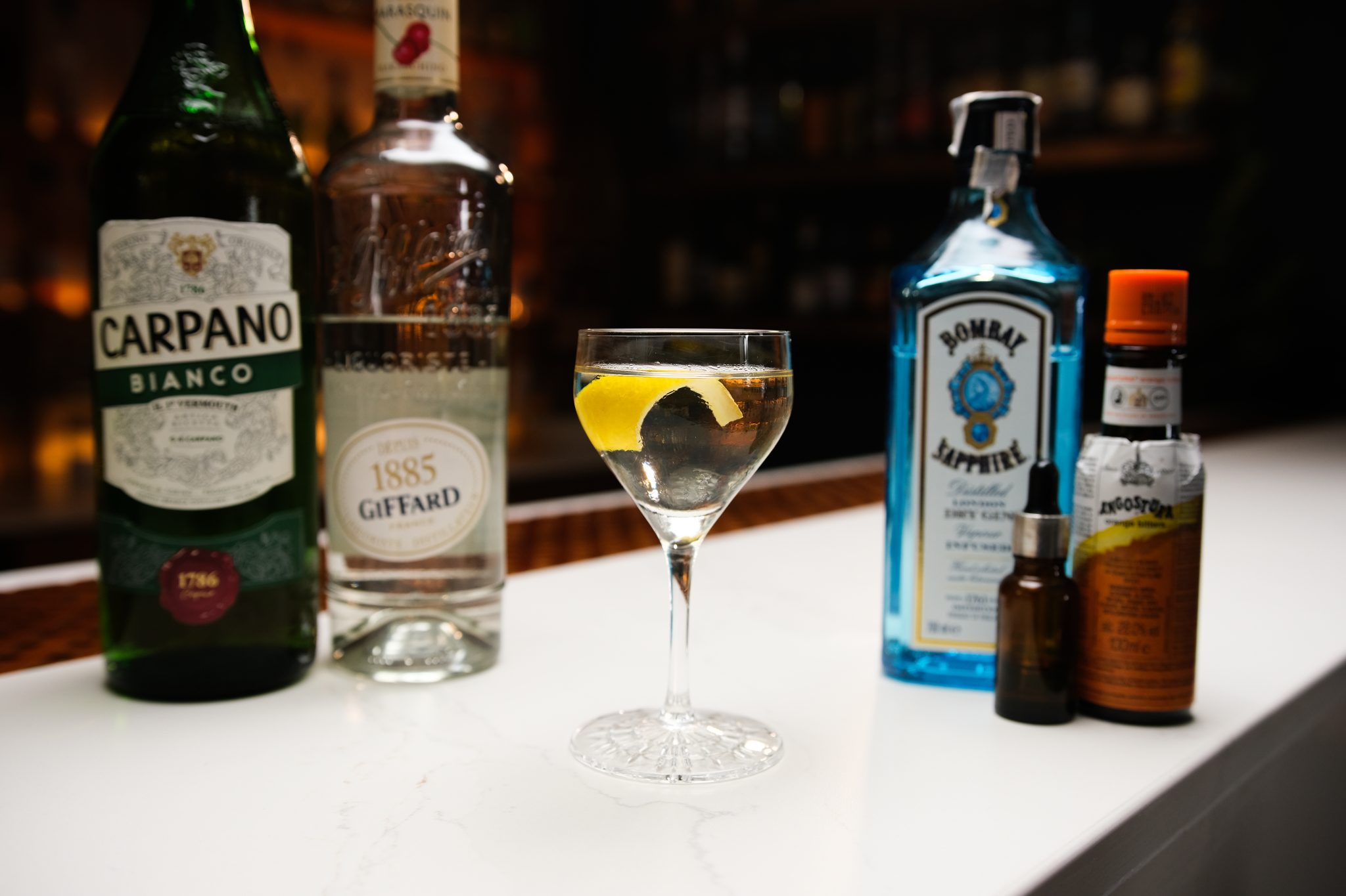 Absinthe, Gin, Dry Vermouth, Maraschino Liqueur, and Orange Bitters laid out on a white bar table.