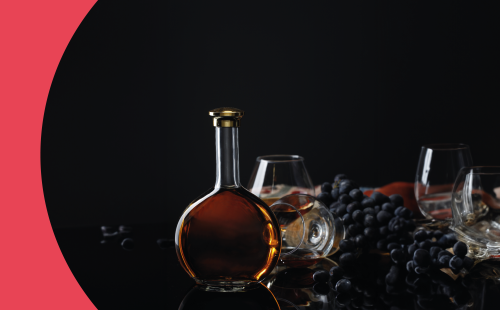 A round bottle of brandy on a black surface with 4 copa glasses and black grapes around