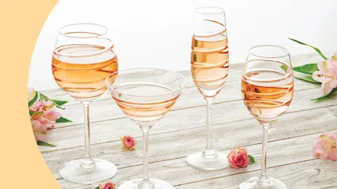 A shot of different types of champagne glasses filled with champagne placed on a light wooden surface and surrounded by small flowers