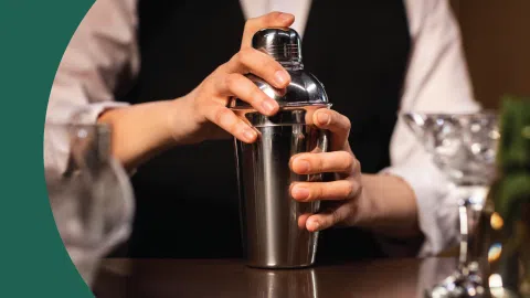 A shot of a bartender holding a cocktail shaker on a dark brown surface