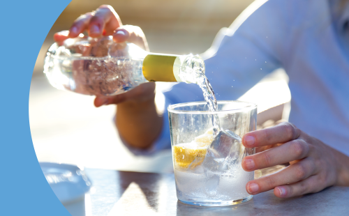 A shot of a person pouring sparkling water in a glass filled with ice cubes and a lemon wedge