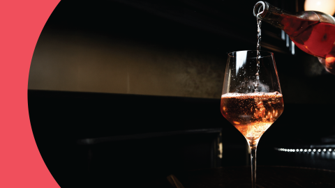A shot of a rose sparkling wine poured into a white wine glass on a black background