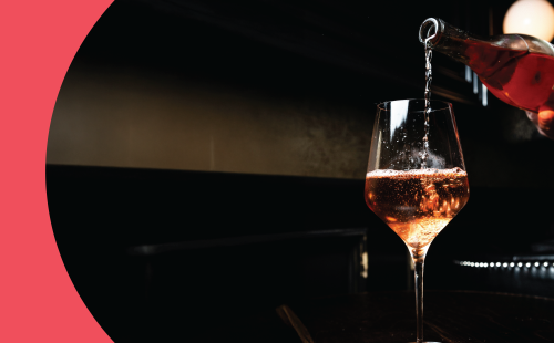 A shot of a rose sparkling wine poured into a white wine glass on a black background