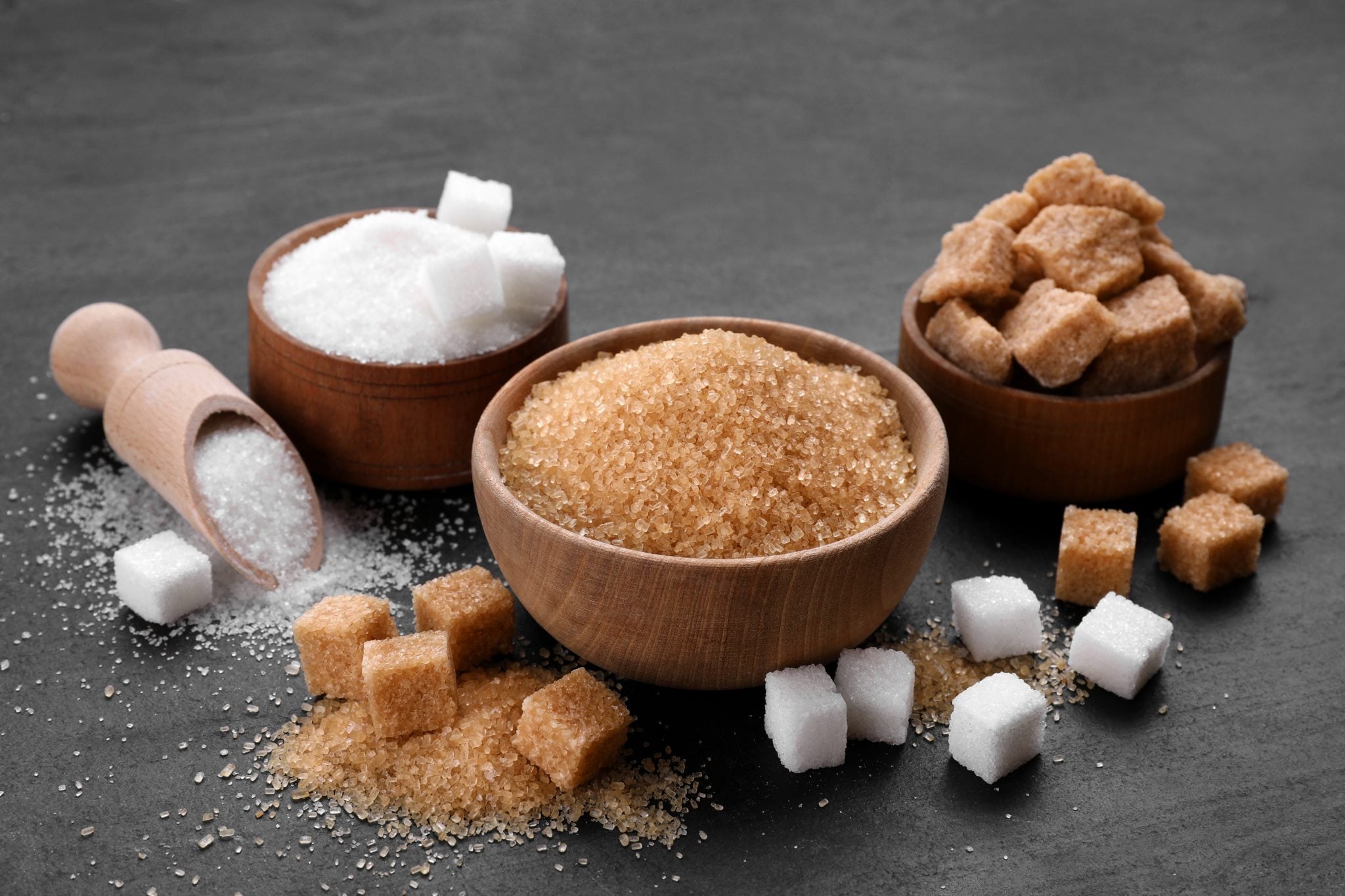 A shot of different types of sugar in different shapes placed on a dark grey surface