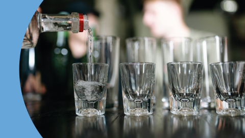 Eight transparent shot glasses in two rows on a black surface been filled with vodka
