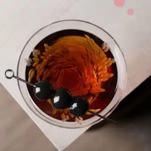 A vermouth glass with three black cherries as garnish, shot from above, placed close to the edge of a table.