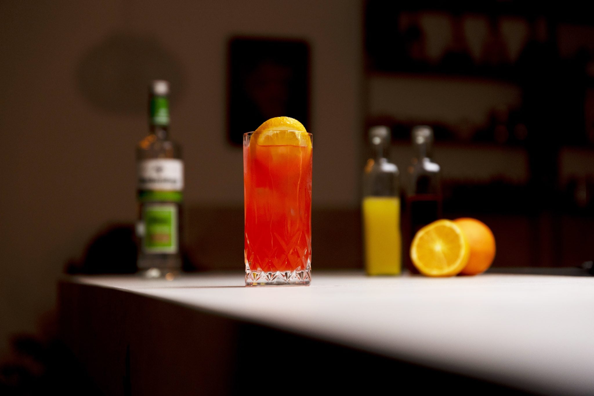 Vodka, orange juice, cranberry juice, and two oranges laid out on a white bar table