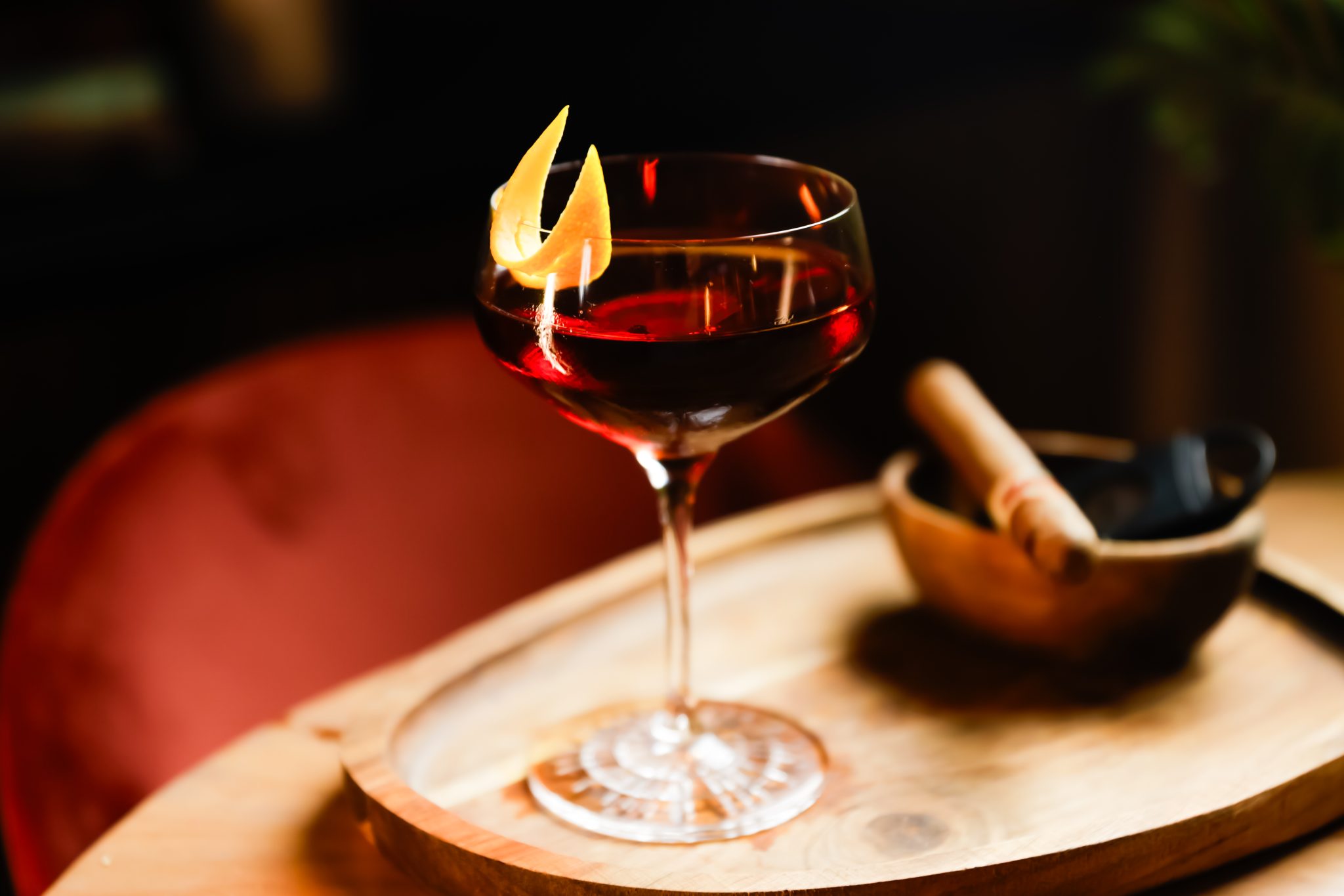 A side shot of a Warsaw cocktail in a coupe glass on a wooden board with a wooden bowl on athe side with a cigar