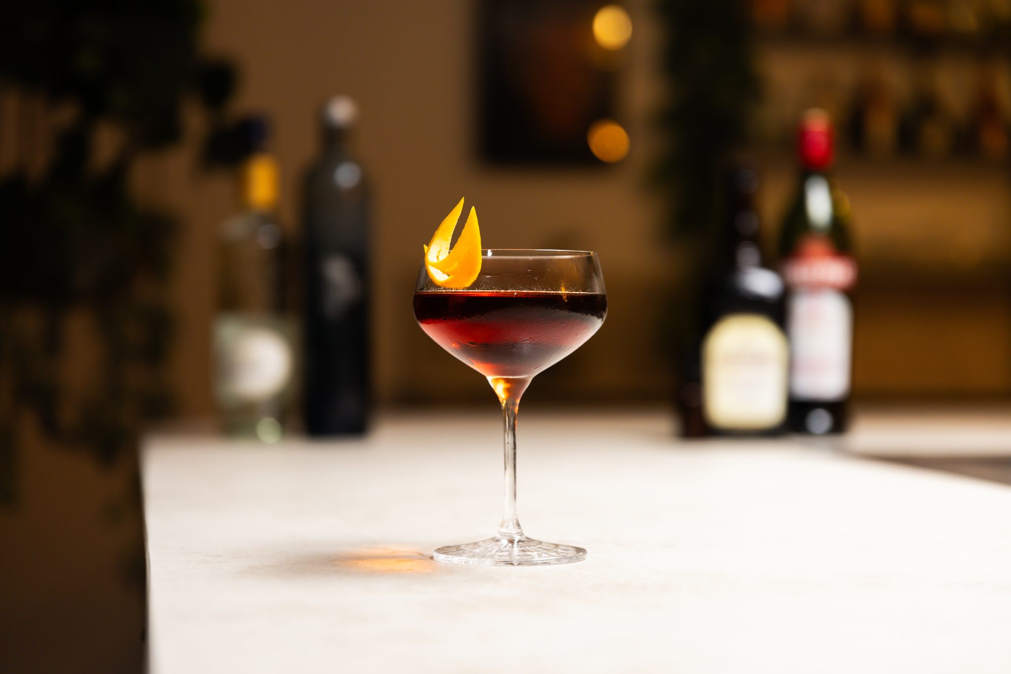 Vodka, sweet vermouth, cherry brandy liqueur, triple sec, and black cherry bitters laid out on a white bar table