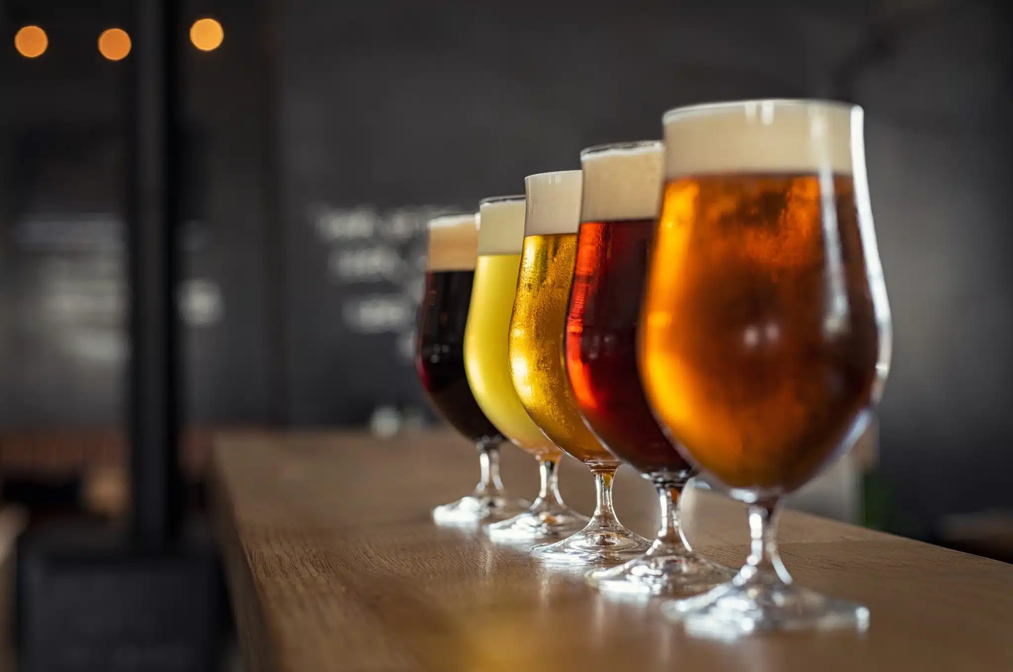 A shot of beer glasses filled with different types of beer on a brown bar table.
