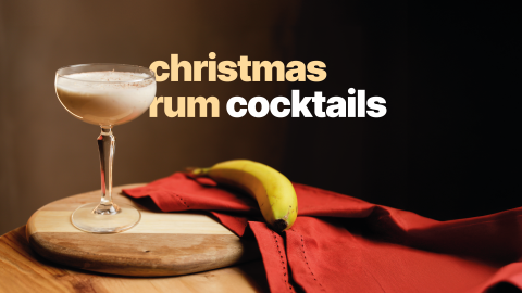 A christmas rum cocktail in a cocktail glass on a wooden board and table surrounded by a red cloth and a banana
