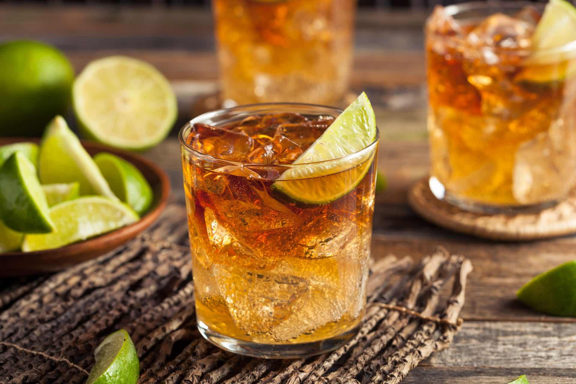 A shot of a Dark "N" Stormy cocktail with rum in an old fashioned glass on table mat with fresh lime wedge as garnish