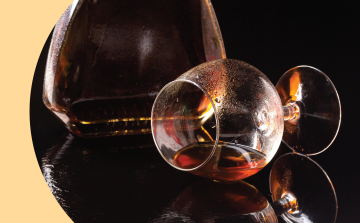 A Liquor bottle and Copa glass lying down with liquor inside on a black background