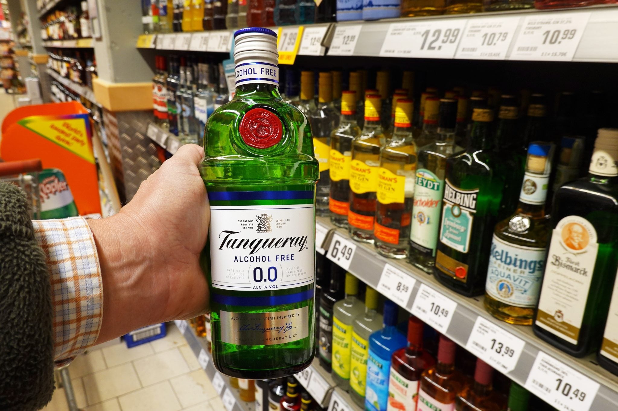 An alcohol free Tanqueray bottle holded by a hand in a supermarket