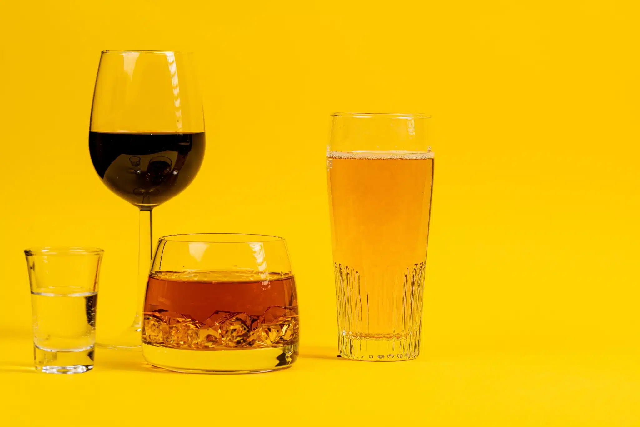A side shot of glasses filled with different types of alcohol with a yellow background color.