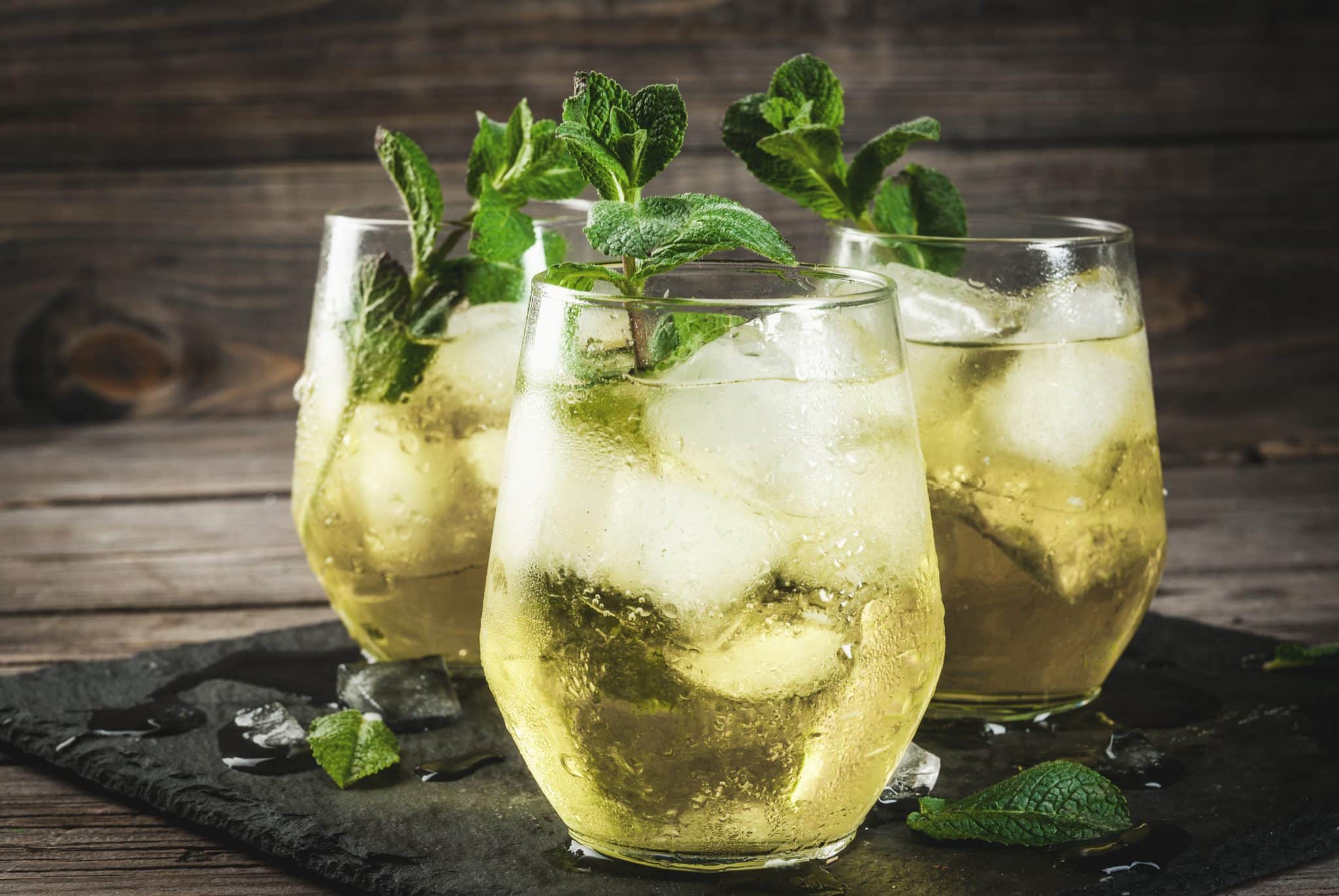 A shot of three Rebujito cocktails with white wine in trumble glasses placed on a black stone tray onj a grey wooden background.